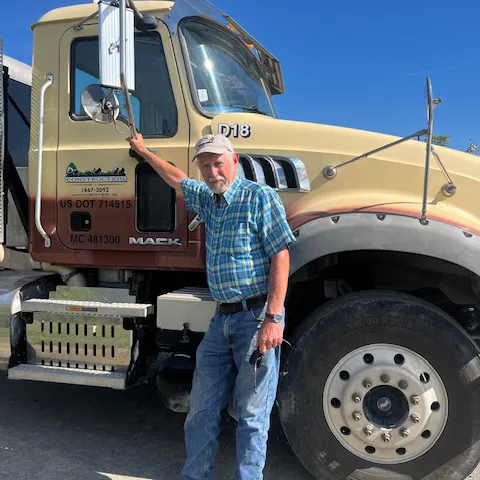 Pine Knoll Construction dump truck driver standing in front of a Pine Knoll Construction dump truck.
