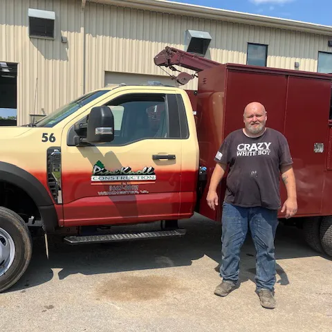 Pine Knoll Construction mechanic standing in front of a pine knoll construction truck.